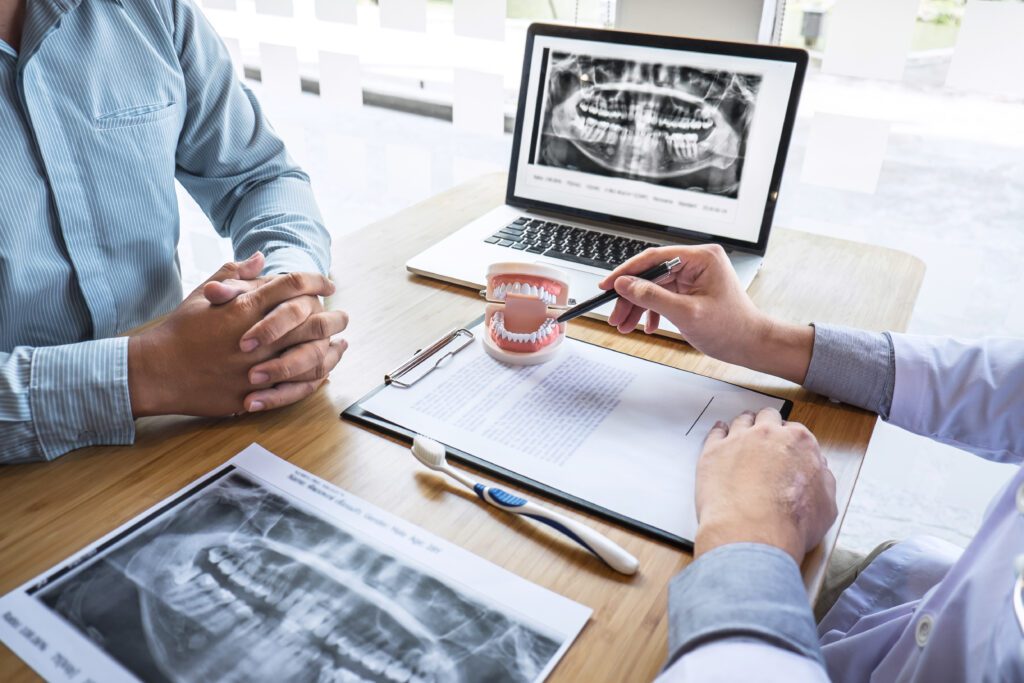 Professional Dentist showing jaw and teeth the x-ray photograph and discussing during explaining the consultation treatment issues with patient and writing history list on report.