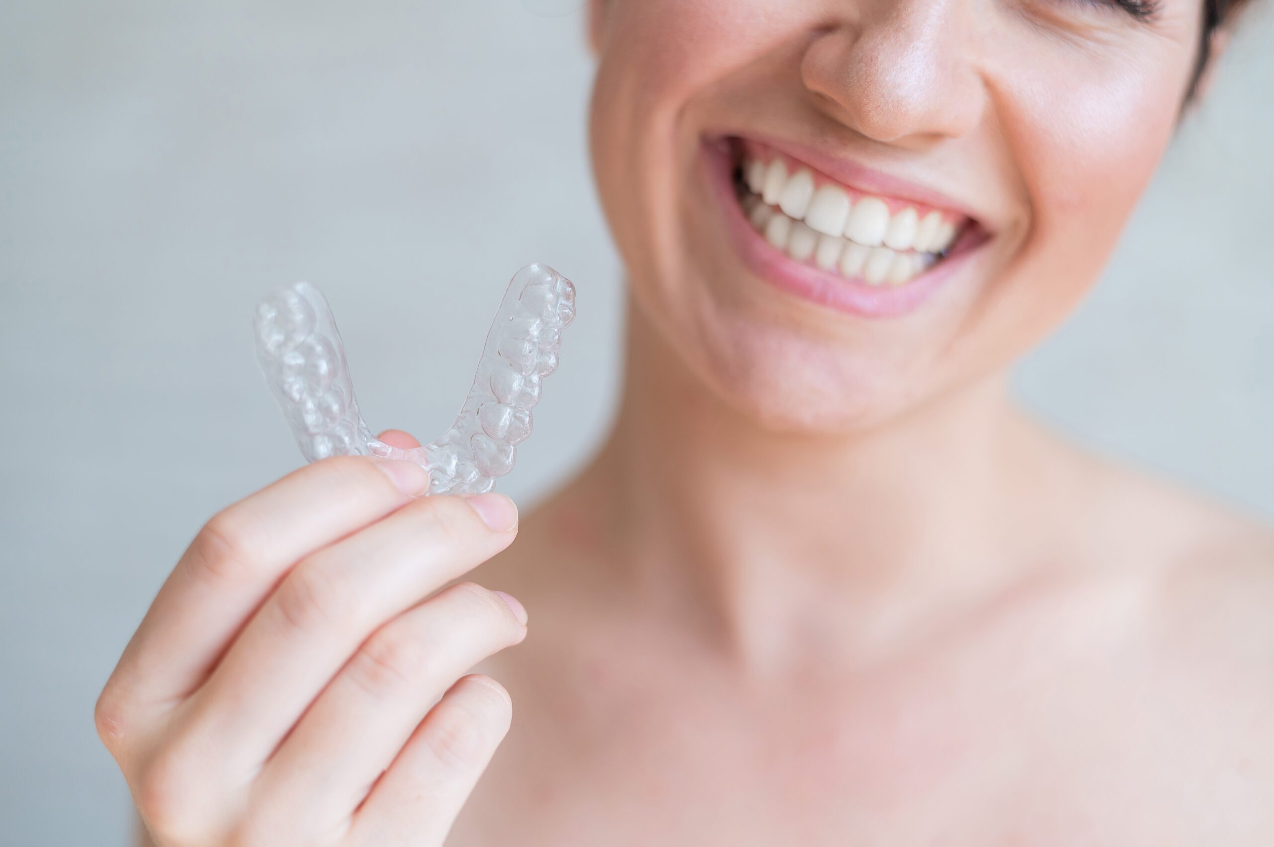 Close-up of orthodontic silicone transparent teeth aligner in female hands. A woman with a perfect charm smile holds a removable night retainer. Bracket for teeth whitening. Cropped photo
