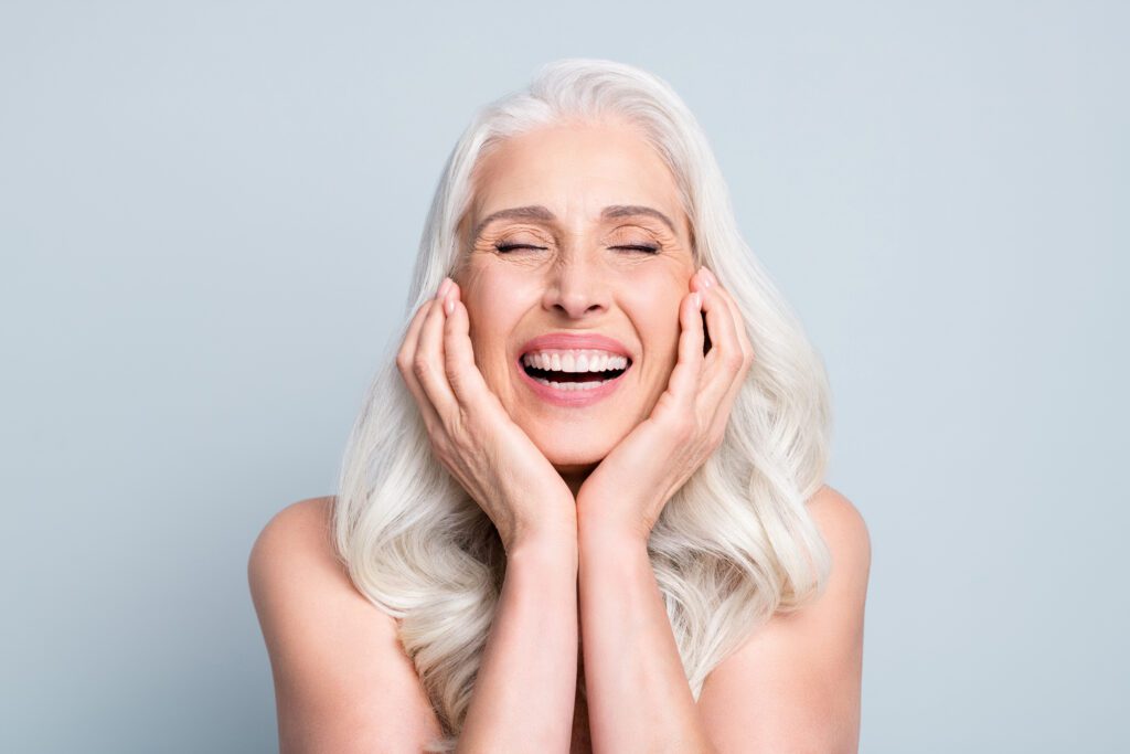 Close-up portrait of her she nice attractive excited cheerful grey-haired elderly lady touching cheeks laughing isolated gray pastel color background.